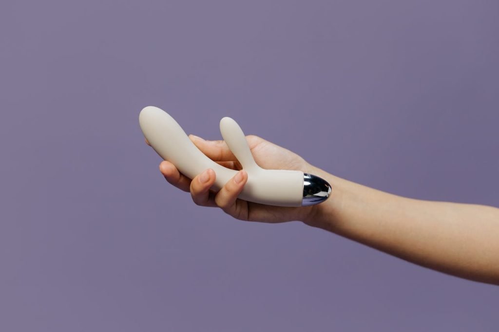 Close-up of a hand holding a dual motor rabbit vibrator against a purple backdrop, emphasizing modern design.