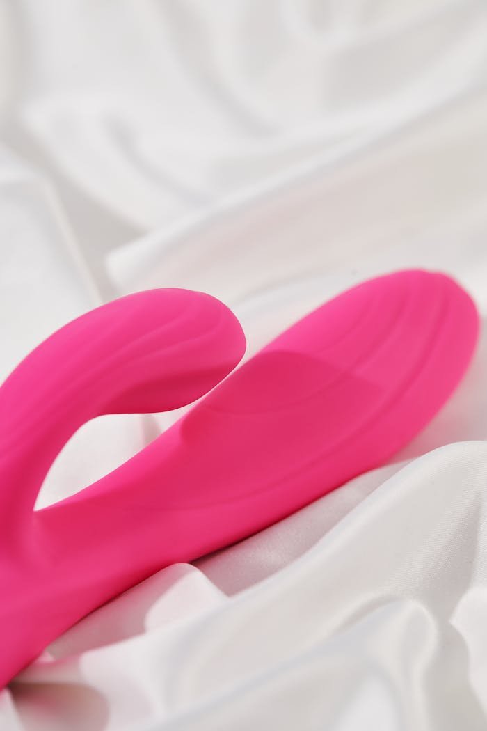 Detailed view of a pink silicone vibrator resting on soft white fabric, emphasizing comfort and elegance.